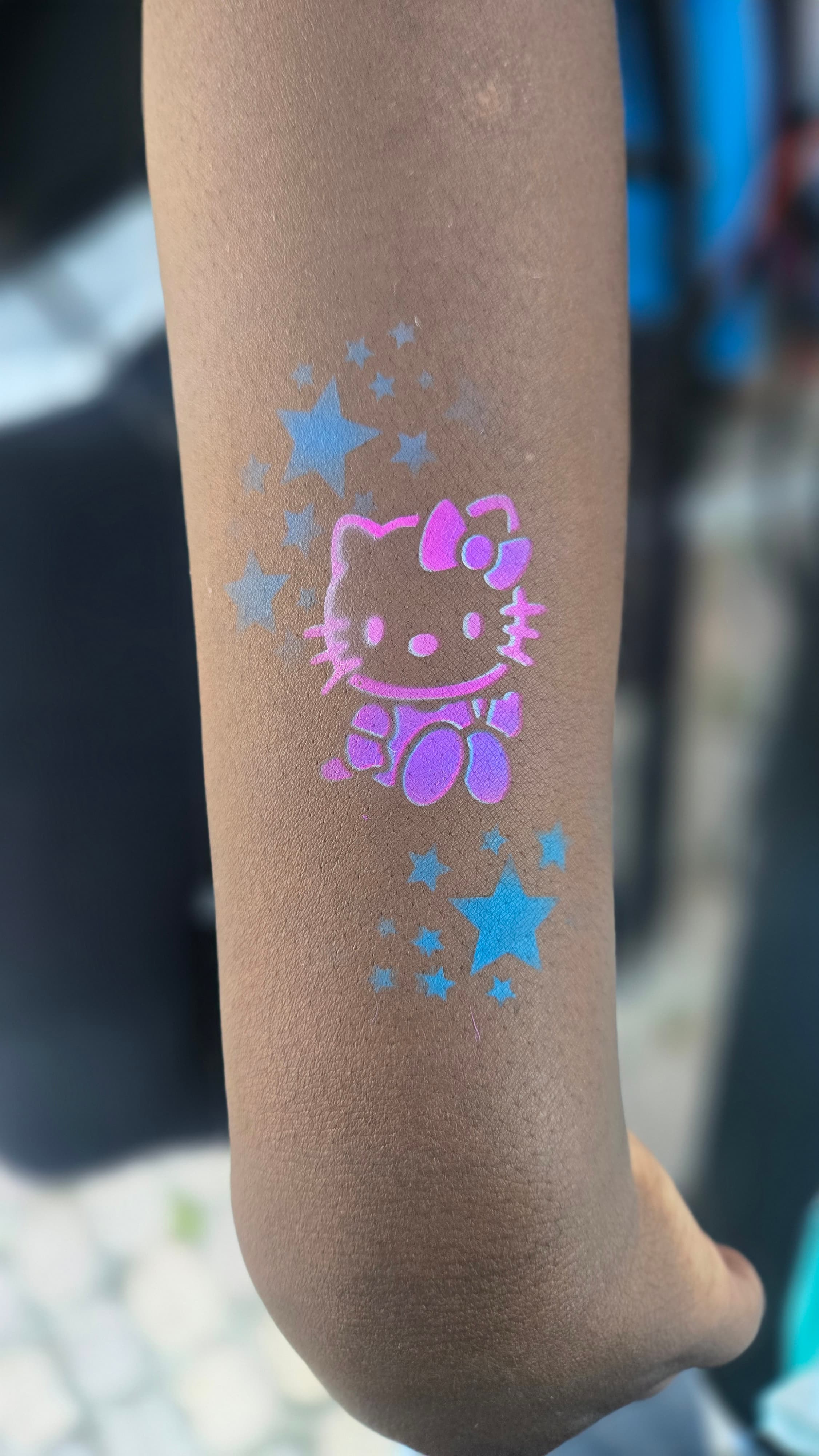 Pink and purple Hello Kitty paint with blue stars on a dark-skinned forearm.