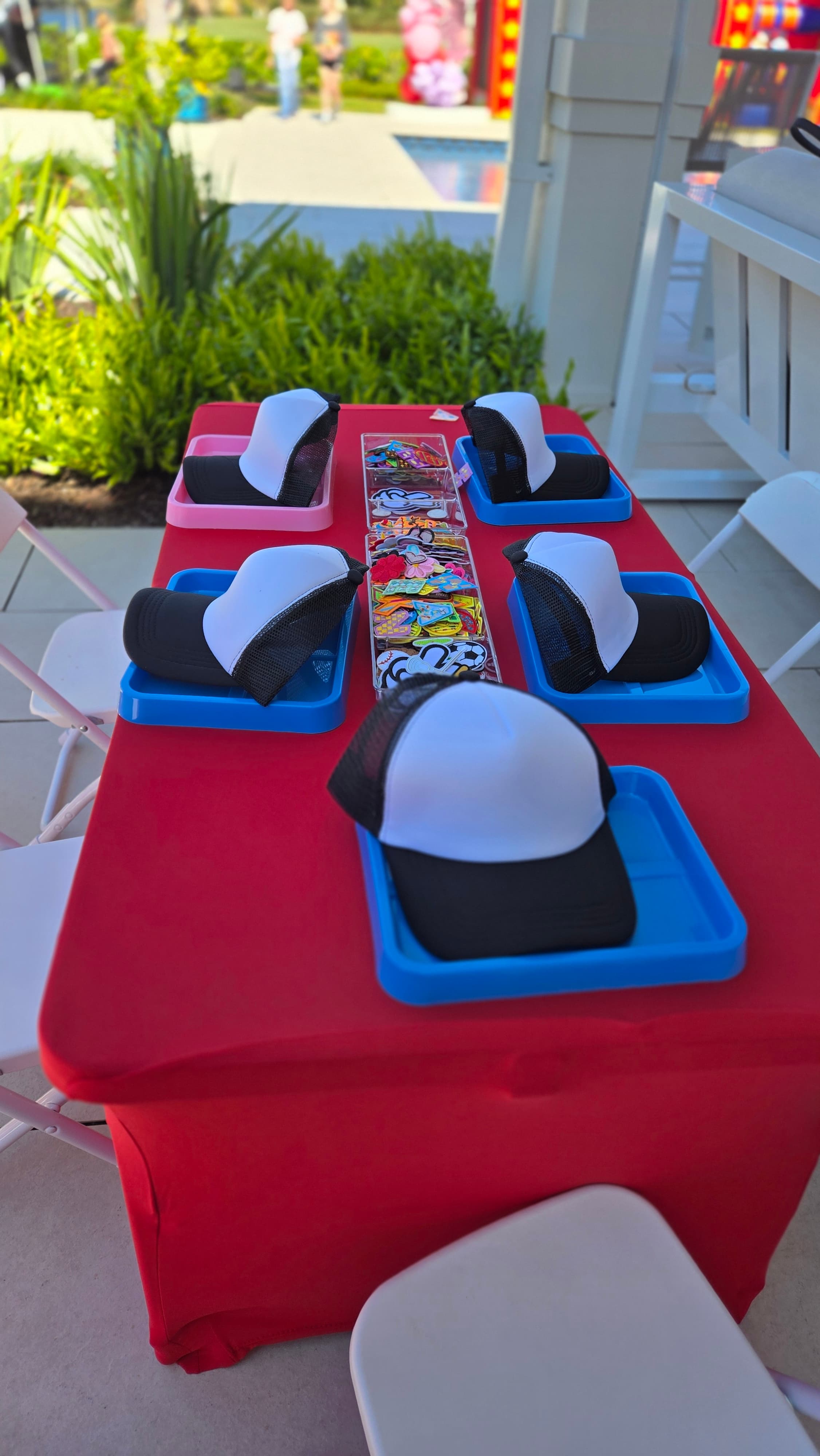 Black and white trucker hats in plastic trays on a red table with colorful patches.